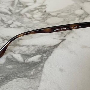 May include: Close-up of sunglasses with a brown tortoiseshell frame and gradient lenses. The arm of the glasses has the model number RB 4378, along with other details. The glasses are set against a marble background.
