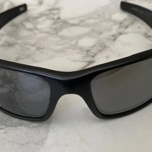 May include: Black sunglasses with a rectangular frame and dark lenses. The sunglasses have a sleek, modern design, suitable for outdoor activities. The lenses appear to be polarized, offering protection from the sun's glare.