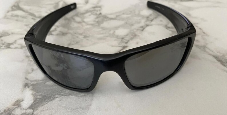 May include: Black sunglasses with a rectangular frame and dark lenses. The sunglasses have a sleek, modern design, suitable for outdoor activities. The lenses appear to be polarized, offering protection from the sun's glare.