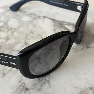 K&ouml;nnte beinhalten: Schwarze Ray-Ban Sonnenbrille mit rechteckigem Rahmen und Farbverlaufsgl&auml;sern. Das Ray-Ban-Logo ist auf dem B&uuml;gel und der Linse zu sehen. Die Sonnenbrille liegt auf einem Marmorhintergrund.