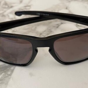 May include: Black sunglasses with a rectangular frame and tinted lenses. The sunglasses have a sleek, modern design, suitable for outdoor activities. The lenses are a dark shade, providing protection from the sun.