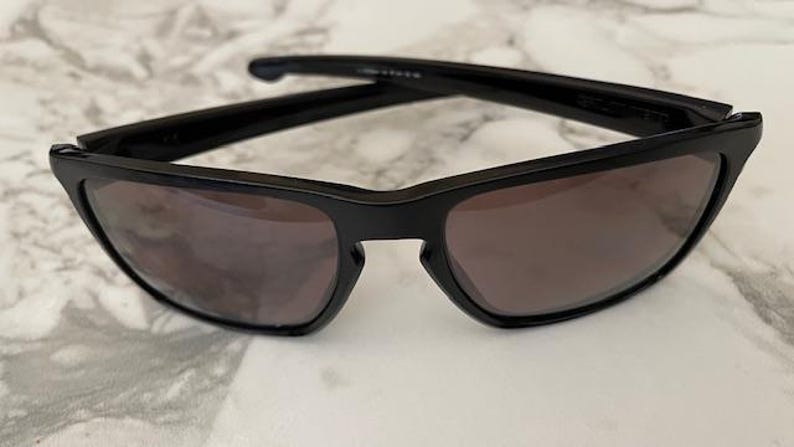 May include: Black sunglasses with a rectangular frame and tinted lenses. The sunglasses have a sleek, modern design, suitable for outdoor activities. The lenses are a dark shade, providing protection from the sun.