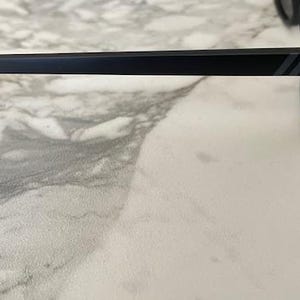 Puede incluir: Un par de gafas de sol negro mate con una patilla recta que presenta dos finas rayas diagonales grises paralelas cerca de la bisagra. La montura est&aacute; fabricada con un material negro s&oacute;lido con lentes oscuras visibles en el lado derecho.