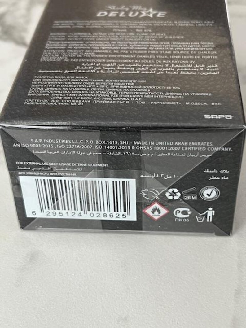 May include: Black rectangular box of "Stately May Deluxe" perfume. The box has text in multiple languages, including English, Arabic, and Ukrainian. It includes a barcode and safety symbols. The product is 4.3 fl oz.