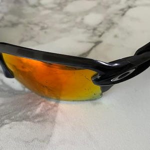 Peut inclure: Lunettes de soleil noires avec verres teint&eacute;s orange. Le design est moderne, avec une monture noire et un logo de la marque sur le c&ocirc;t&eacute;. Les verres sont r&eacute;fl&eacute;chissants.