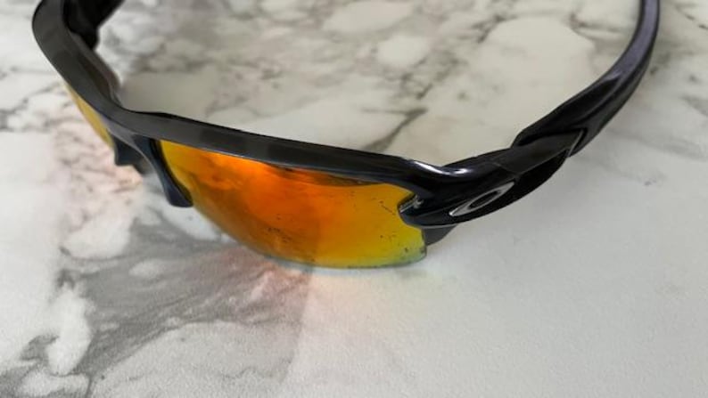 Peut inclure: Lunettes de soleil noires avec verres teint&eacute;s orange. Le design est moderne, avec une monture noire et un logo de la marque sur le c&ocirc;t&eacute;. Les verres sont r&eacute;fl&eacute;chissants.