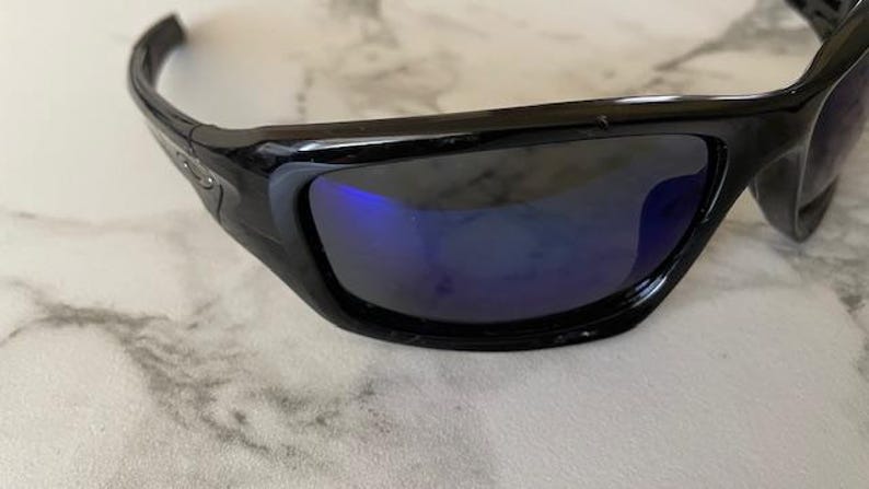 May include: Black sunglasses with a curved frame and blue-tinted lenses. The sunglasses have a sleek, modern design, suitable for outdoor activities. The lenses reflect a blue hue.