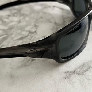 May include: Close-up of black sunglasses with dark lenses. The sunglasses have a sleek, curved design with a glossy finish. The frame appears to be made of a durable material, and the lenses are tinted to reduce glare.