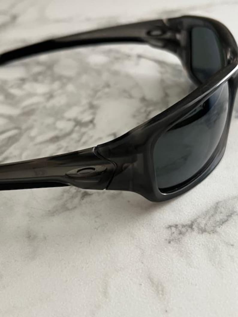 May include: Close-up of black sunglasses with dark lenses. The sunglasses have a sleek, curved design with a glossy finish. The frame appears to be made of a durable material, and the lenses are tinted to reduce glare.