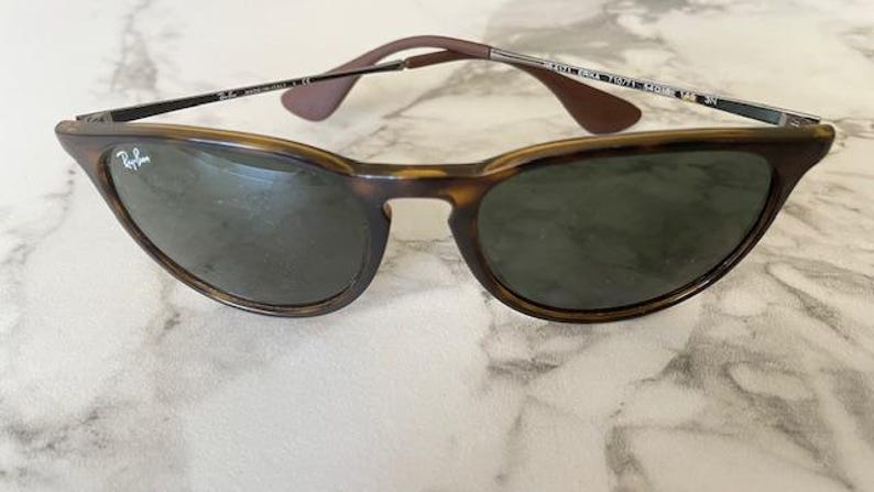 K&ouml;nnte beinhalten: Sonnenbrille mit Schildpatt-Fassung und dunklen Gl&auml;sern. Die Sonnenbrille hat eine klassische Cat-Eye-Form mit einem braun-schwarzen Muster auf den Fassungen. Die B&uuml;gel sind dunkelbraun und die Gl&auml;ser sind dunkelgr&uuml;n.