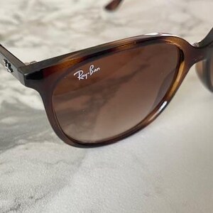 May include: Brown tortoiseshell sunglasses with gradient lenses. The Ray-Ban logo is visible on the right lens. The sunglasses have a classic, slightly oversized frame design.