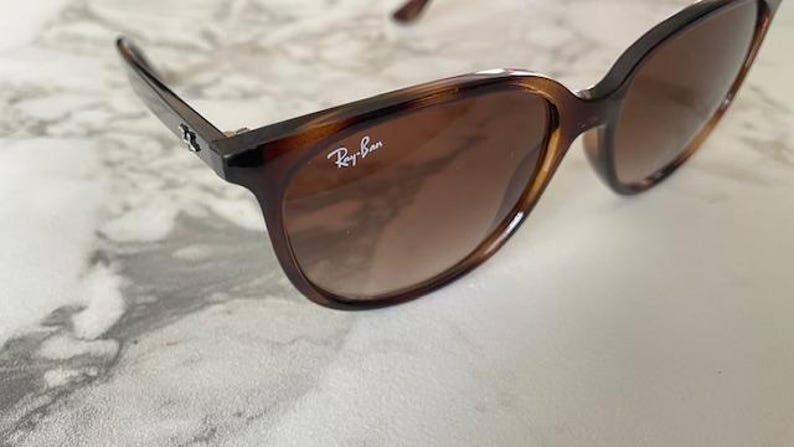 May include: Brown tortoiseshell sunglasses with gradient lenses. The Ray-Ban logo is visible on the right lens. The sunglasses have a classic, slightly oversized frame design.