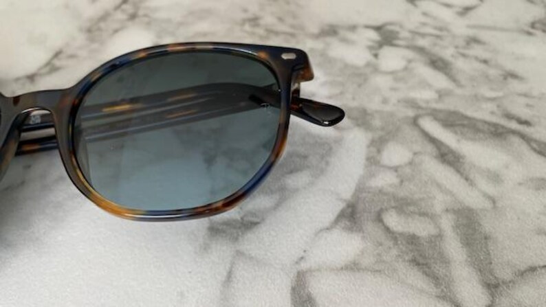 May include: Sunglasses with a tortoiseshell pattern frame and blue-tinted lenses. The frame features a mix of brown, orange, and dark blue hues. The sunglasses have a classic, rounded shape, suitable for various face shapes.