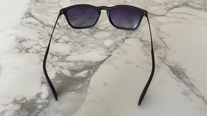 May include: Black sunglasses with a square frame and gradient lenses. The sunglasses have a sleek, modern design with thin temples. The lenses transition from a darker shade at the top to a lighter shade at the bottom.