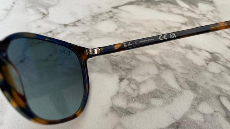 May include: Sunglasses with blue lenses and a tortoiseshell pattern on the frames. The temples have a dark blue and brown pattern. The Ray-Ban logo is visible on the temple and lens.