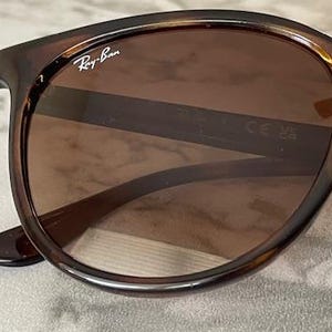 May include: Brown Ray-Ban sunglasses with a tortoiseshell frame. The lenses are a gradient brown color. The Ray-Ban logo is visible on the upper left corner of the frame.
