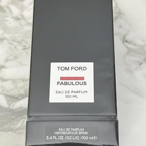 May include: A black rectangular box of Tom Ford Fabulous Eau de Parfum. The white label reads "TOM FORD" above "FABULOUS" with a red bar. Below it is "EAU DE PARFUM 100 ML". The bottom label reads "EAU DE PARFUM VAPORISATEUR SPRAY 100 ml e".