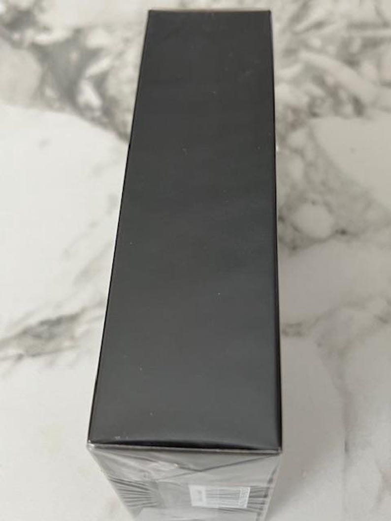 K&ouml;nnte beinhalten: Gezeigt wird eine rechteckige, schwarze Schachtel, vermutlich f&uuml;r Verpackungszwecke. Die Schachtel ist in klarem Kunststoff verpackt, und die Oberseite und die Seiten sind einfarbig matt schwarz. Die Schachtel steht vertikal auf einer hellen, marmorierten Oberfl&auml;che.