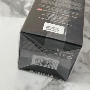May include: A black rectangular box with text and a barcode. The box is labeled "DESIGNED AND DEVELOPED IN USA" and includes contact information for the manufacturer. The expiration date is printed on a white sticker.