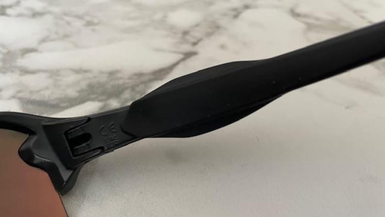 Puede incluir: Primer plano de gafas de sol negras con acabado mate. La montura tiene un dise&ntilde;o elegante y moderno con una patilla curva. Las lentes tienen un tinte degradado y el &aacute;rea de la bisagra muestra una marca CE.