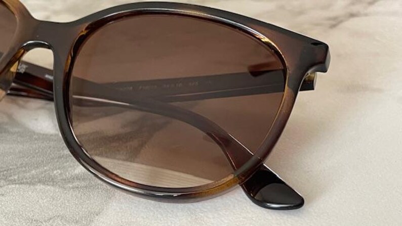 May include: Brown tortoiseshell sunglasses with brown tinted lenses. The frames have a rounded shape and a glossy finish. The arms of the sunglasses are dark brown and have a slight curve. The lenses are a medium brown color.