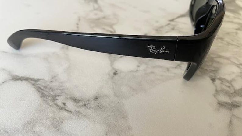 Puede incluir: Gafas de sol negras con el logotipo de Ray-Ban en la patilla. Las gafas de sol tienen un dise&ntilde;o elegante y moderno con un acabado brillante. Las monturas son gruesas y las lentes oscuras, ofreciendo protecci&oacute;n solar.