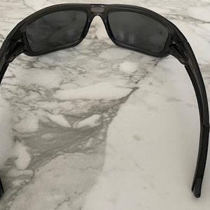 May include: Black sunglasses with dark tinted lenses. The sunglasses have a sleek, modern design with a curved frame and arms. The lenses are rectangular and the frame is a glossy black color.