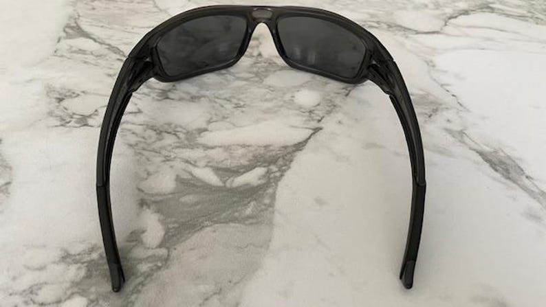 May include: Black sunglasses with dark tinted lenses. The sunglasses have a sleek, modern design with a curved frame and arms. The lenses are rectangular and the frame is a glossy black color.