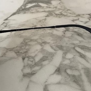 Puede incluir: Gafas de sol negras con acabado mate. Las monturas son cuadradas con lentes degradadas. Las patillas son finas y se curvan en la oreja. Las gafas de sol est&aacute;n sobre una superficie de m&aacute;rmol.