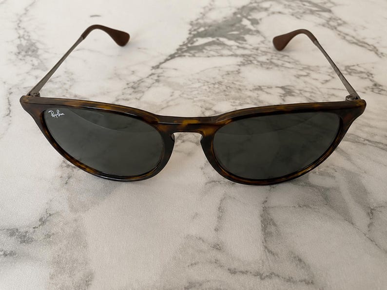 K&ouml;nnte beinhalten: Sonnenbrille mit Schildpattmuster und dunklen Gl&auml;sern. Die Fassungen sind braun und schwarz, mit d&uuml;nnen Metallb&uuml;geln und braunen Ohrenteilen. Das Ray-Ban-Logo ist auf dem linken Glas sichtbar.