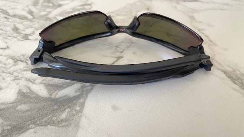 Peut inclure: Lunettes de soleil noires avec une monture incurv&eacute;e et des verres teint&eacute;s. Les lunettes sont pli&eacute;es, mettant en valeur le design &eacute;pur&eacute; et les charni&egrave;res. Les verres ont une teinte d&eacute;grad&eacute;e, passant d'une teinte plus fonc&eacute;e en haut &agrave; une plus claire en bas.