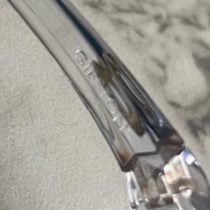 May include: Close-up of a clear plastic object with the word "GIBSON" embossed on the side. The object has a curved shape and appears to be part of a larger item. The background is a blurred, light-colored surface.