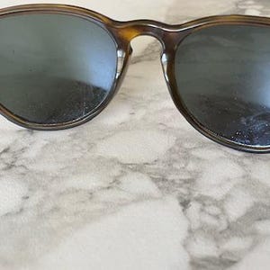K&ouml;nnte beinhalten: Runde Sonnenbrille mit Schildpattmuster. Die Gl&auml;ser sind dunkel und die Fassungen sind eine Mischung aus Braun und Beige. Die Sonnenbrille hat einen klassischen, Vintage-Look.