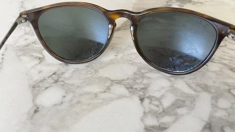 K&ouml;nnte beinhalten: Runde Sonnenbrille mit Schildpattmuster. Die Gl&auml;ser sind dunkel und die Fassungen sind eine Mischung aus Braun und Beige. Die Sonnenbrille hat einen klassischen, Vintage-Look.