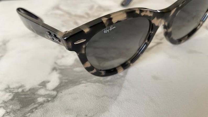 Puede incluir: Gafas de sol con estampado de carey y lentes oscuras. Las gafas de sol tienen un dise&ntilde;o cl&aacute;sico con una montura gruesa y el logotipo de Ray-Ban visible en la lente. Las patillas tambi&eacute;n tienen un estampado.