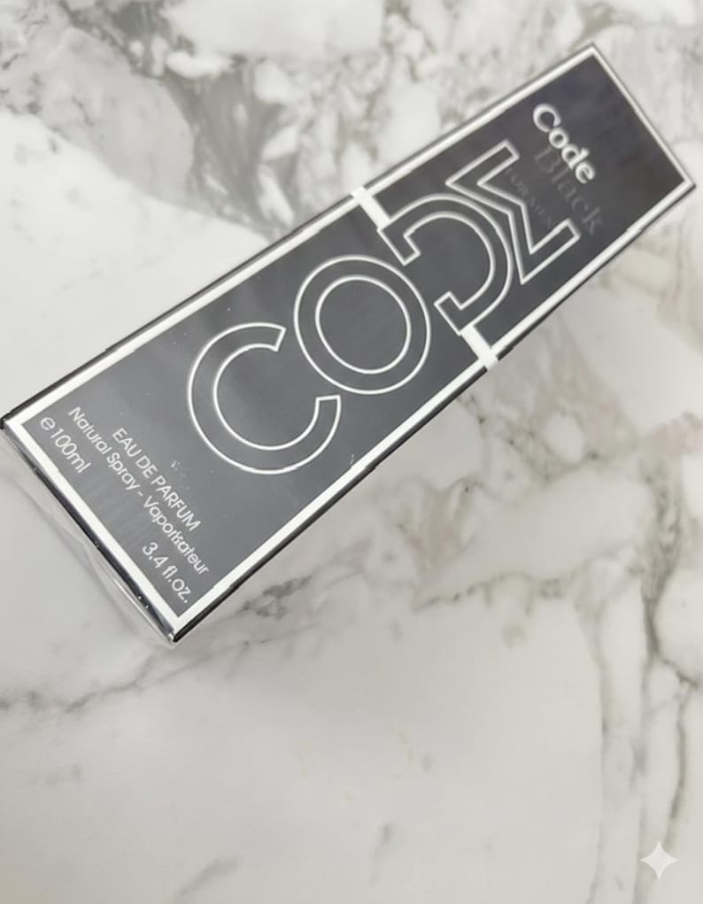 May include: A rectangular black perfume box with the text "Code Black" and "CO52" in a silver, bold font. The box also includes the text "EAU DE PARFUM" and "3.4 fl.oz.". The box is set against a marble background.