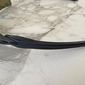 Peut inclure: Gros plan sur des lunettes de soleil de sport noires avec une branche incurv&eacute;e. Les lunettes ont un logo blanc sur la monture et un verre fonc&eacute;. La monture est en mat&eacute;riau noir mat. Les lunettes sont con&ccedil;ues pour le sport et les activit&eacute;s de plein air.
