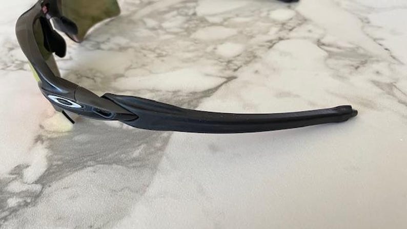 Peut inclure: Gros plan sur des lunettes de soleil de sport noires avec une branche incurv&eacute;e. Les lunettes ont un logo blanc sur la monture et un verre fonc&eacute;. La monture est en mat&eacute;riau noir mat. Les lunettes sont con&ccedil;ues pour le sport et les activit&eacute;s de plein air.