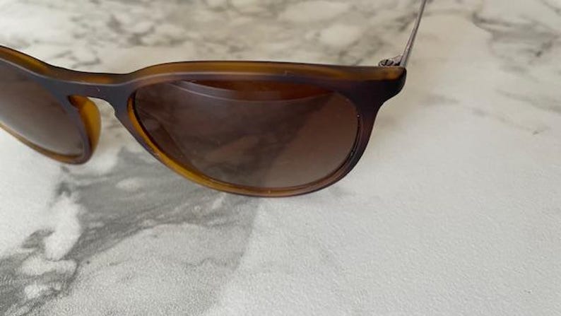 May include: Brown sunglasses with a classic design. The frames are a warm brown color, and the lenses are a darker shade of brown. The sunglasses are resting on a white surface.