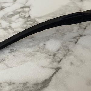 Peut inclure: Gros plan sur des lunettes de soleil noires avec une branche incurv&eacute;e. Les lunettes de soleil ont un design &eacute;l&eacute;gant et moderne. Les verres sont de couleur marron clair. La monture est noire.