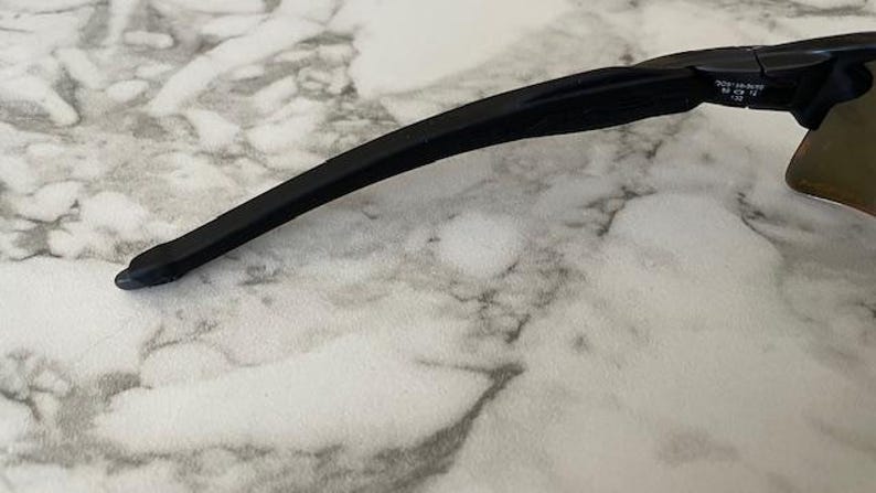 Peut inclure: Gros plan sur des lunettes de soleil noires avec une branche incurv&eacute;e. Les lunettes de soleil ont un design &eacute;l&eacute;gant et moderne. Les verres sont de couleur marron clair. La monture est noire.