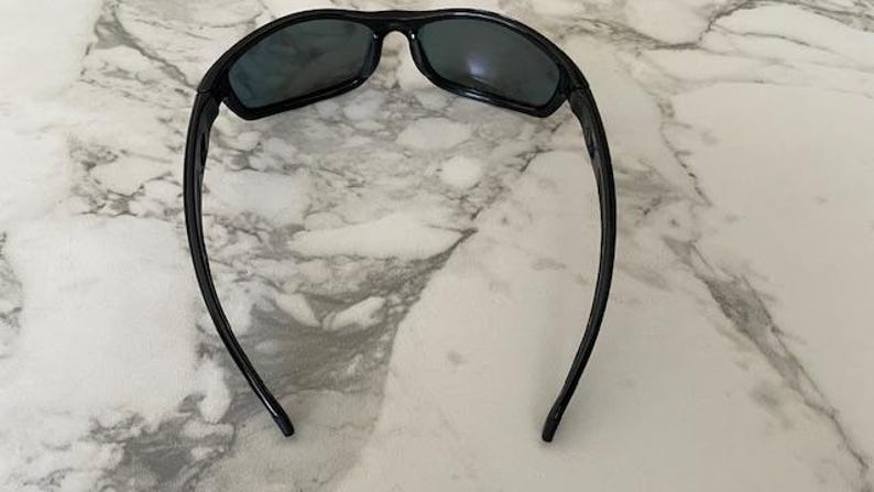 May include: Black sunglasses with a curved frame and dark lenses. The sunglasses are designed for sports or outdoor activities. The arms of the sunglasses curve down and away from the lenses.