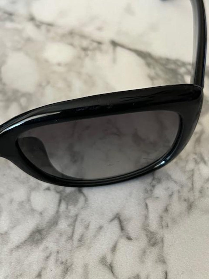 K&ouml;nnte beinhalten: Schwarze Cat-Eye-Sonnenbrille mit dunkel get&ouml;nten Gl&auml;sern. Die Sonnenbrille hat ein schlankes, modernes Design mit gl&auml;nzendem Finish. Der Rahmen ist dick und kantig.