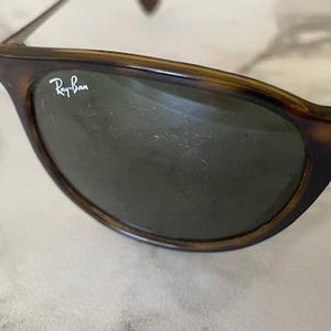 K&ouml;nnte beinhalten: Nahaufnahme einer Ray-Ban Sonnenbrille mit Schildpatt-Fassung und dunklen Gl&auml;sern. Das Ray-Ban-Logo ist auf dem oberen linken Glas zu sehen. Die Sonnenbrille befindet sich vor einem hellen Hintergrund.