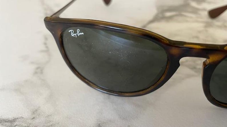 K&ouml;nnte beinhalten: Nahaufnahme einer Ray-Ban Sonnenbrille mit Schildpatt-Fassung und dunklen Gl&auml;sern. Das Ray-Ban-Logo ist auf dem oberen linken Glas zu sehen. Die Sonnenbrille befindet sich vor einem hellen Hintergrund.