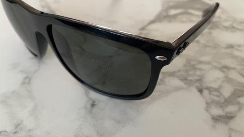 Puede incluir: Gafas de sol negras con lentes oscuras. Las gafas tienen un dise&ntilde;o de montura rectangular cl&aacute;sico. Las patillas presentan un acento plateado cerca de las bisagras. Las lentes son oscuras, proporcionando sombra y protecci&oacute;n solar.