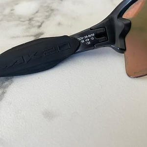 Peut inclure: Gros plan sur des lunettes de soleil noires avec le logo FLAK 2.0 sur la branche. Les verres sont de couleur marron d&eacute;grad&eacute;. La monture porte les chiffres 58 12 et 133 sur la branche.