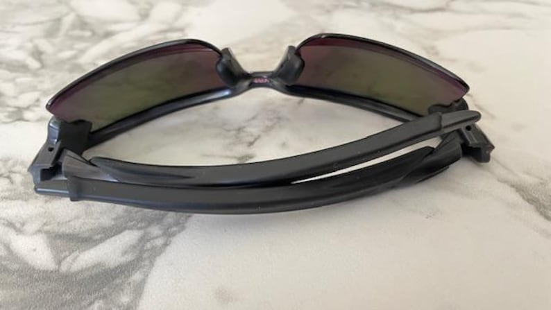 Puede incluir: Gafas de sol negras con montura curvada y lentes tintadas. Las gafas de sol est&aacute;n plegadas, mostrando las bisagras y el interior de las patillas. Las lentes tienen un tinte degradado, que pasa de un color m&aacute;s oscuro en la parte superior a un tono m&aacute;s claro.