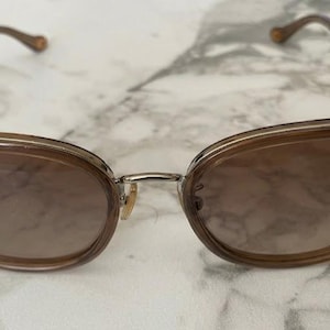 May include: Cat-eye sunglasses with a light brown frame and gradient lenses. The frames are a translucent brown with a silver bridge and brown temples. The lenses transition from a darker brown at the top to a lighter shade at the bottom.