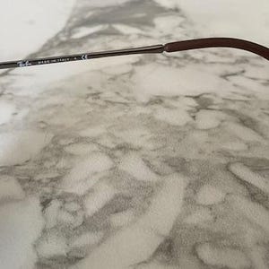 K&ouml;nnte beinhalten: Nahaufnahme einer Sonnenbrille. Der Rahmen hat ein Schildpattmuster mit dunklen Gl&auml;sern. Der B&uuml;gel ist silberfarben mit dem Text "MADE IN ITALY" und einem braunen Ohrb&uuml;gel.